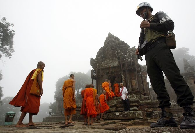Monks walk past a soldier to attend a Buddhism ceremony praying for peace called Krong Pealy at Preah Vihear temple compound atop Dang Reak mountain